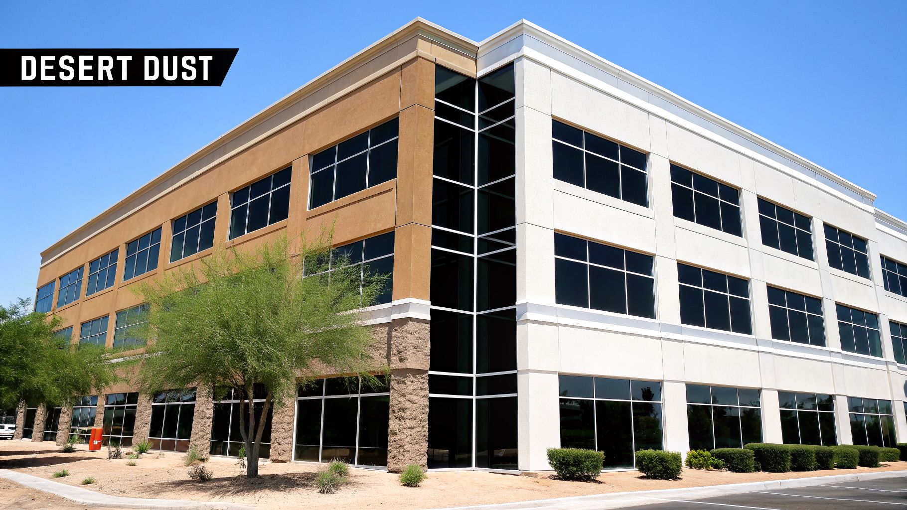 A modern commercial building with brown and white sections, large windows, and desert trees under a blue sky.